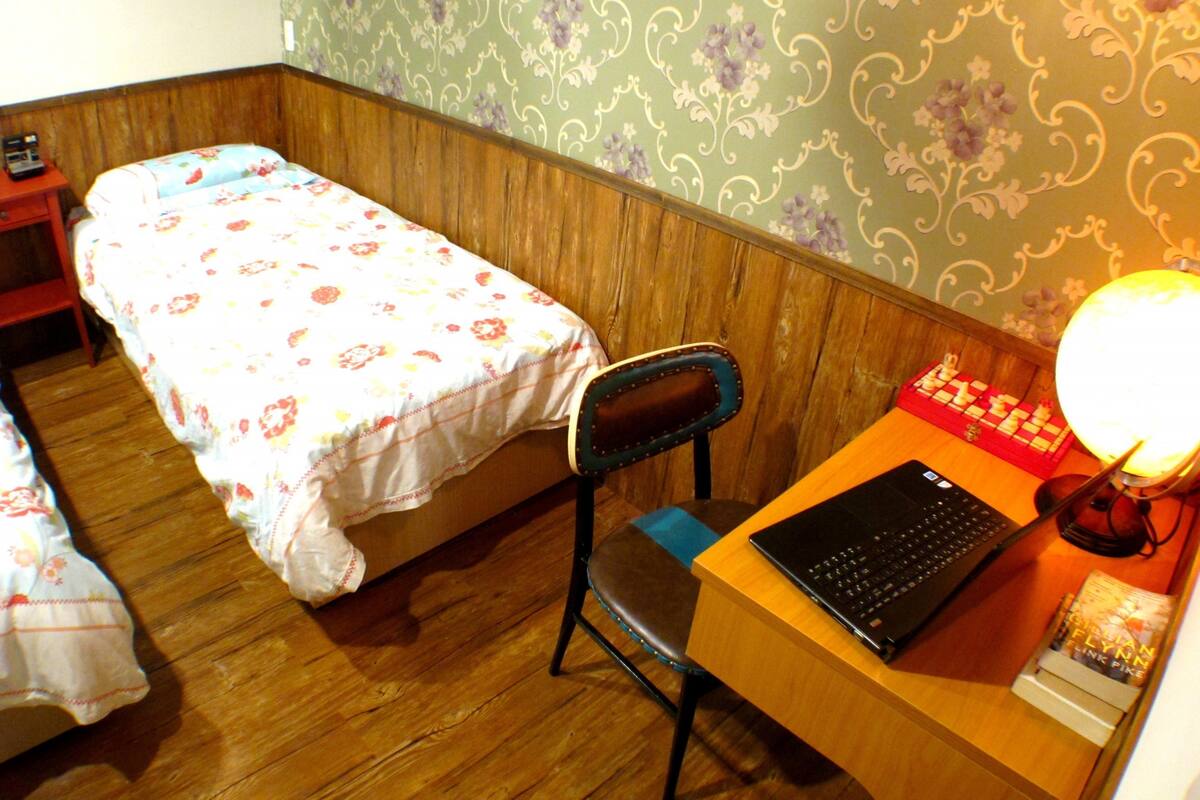A small room with a bed, a desk with a laptop, and a chair.