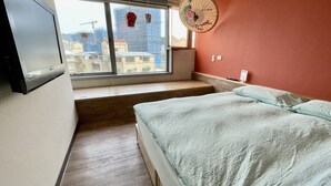Ein Schlafzimmer mit Bett, Fenster, Ventilator und an der Wand montiertem Fernseher.
