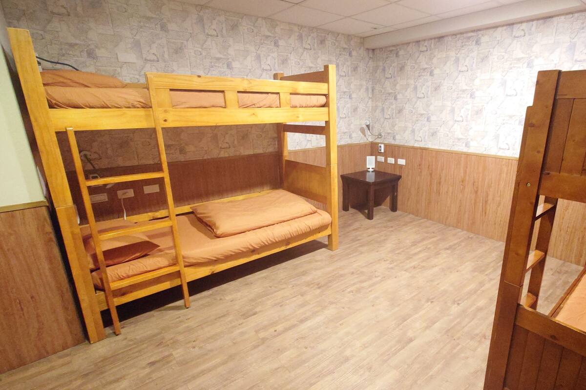 A bunk bed room with wooden bunk beds and a small wooden table.