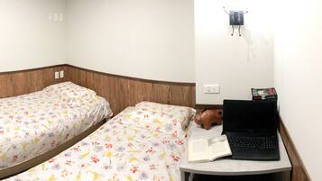 A room with two beds, a small table with a laptop and a book, and a wall-mounted light fixture.