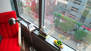 Ein modernes Zimmer mit einem roten Sessel, einem Schreibtisch mit Lampe und einem Fenster mit Blick auf eine Skyline.
