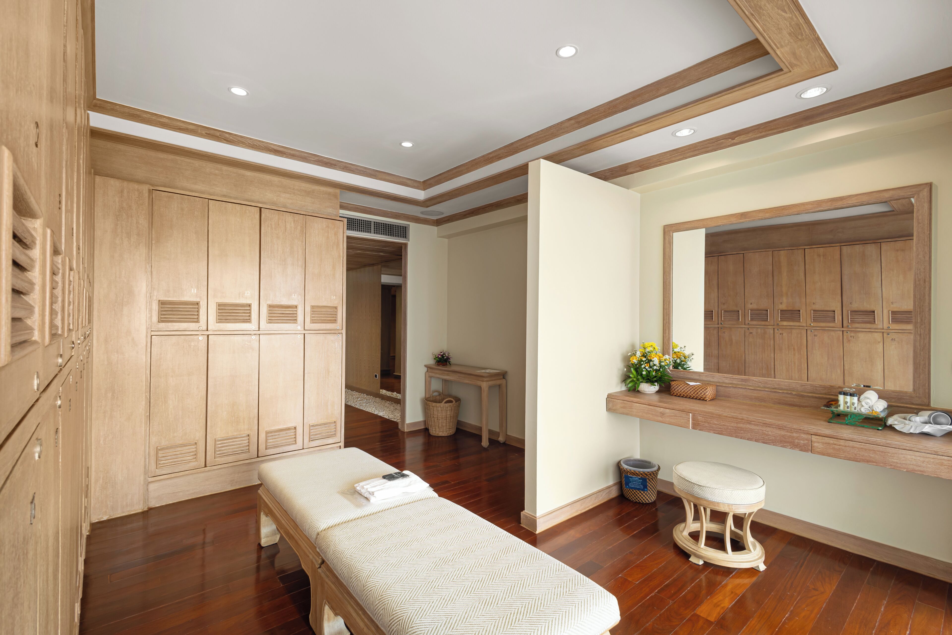 A room with wooden cabinets, a bench, a small table with a basket, and a mirror on the wall.