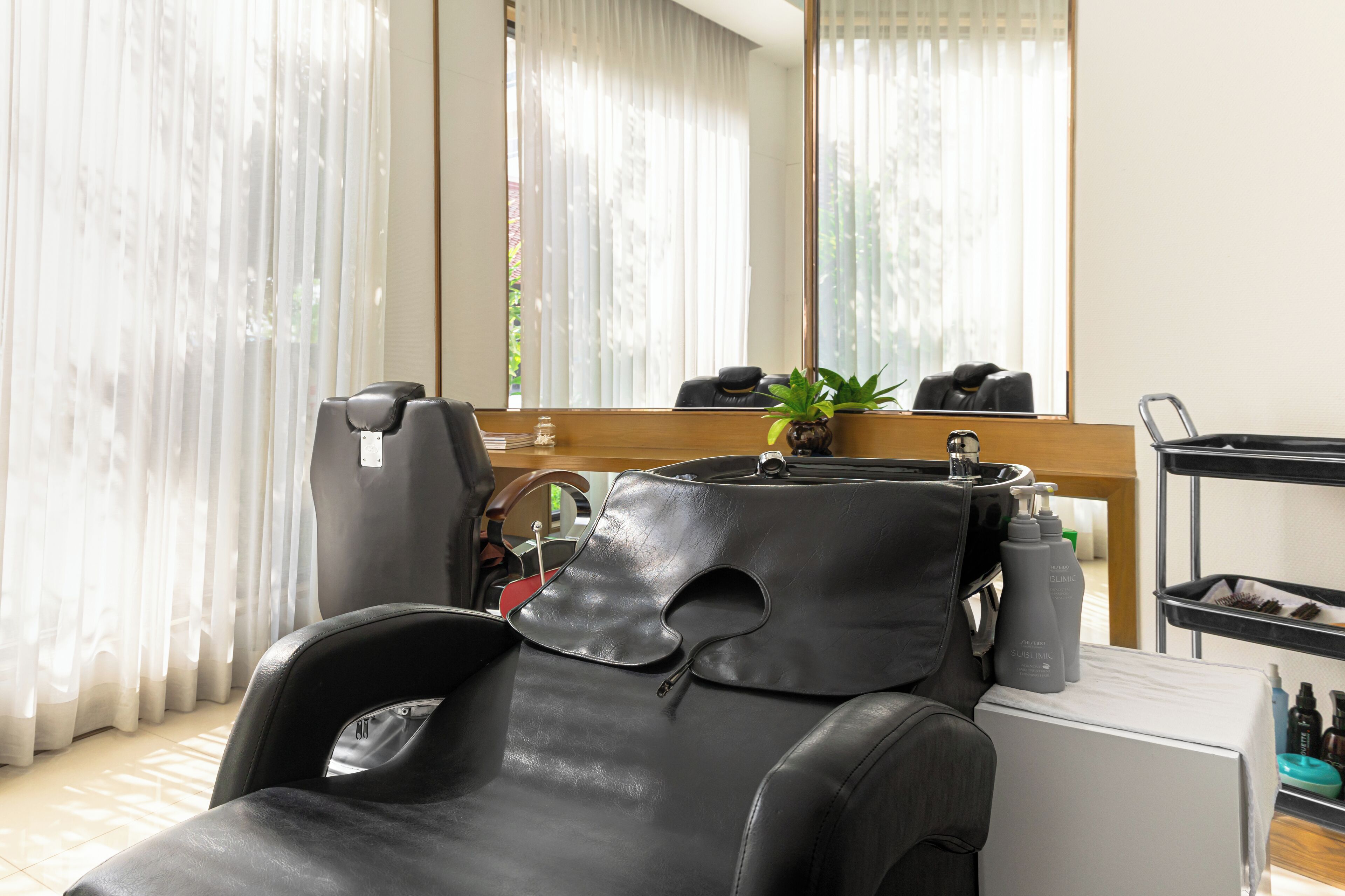 A modern hair salon with a leather massage chair, a large mirror, and a small plant.