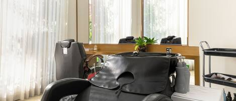 A modern hair salon with a leather massage chair, a large mirror, and a small plant.