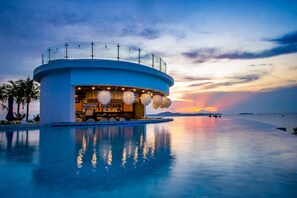 Un bar frente al agua con piscina y vistas al atardecer.