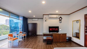 A hotel room with a large window, a desk with a TV, a chair, a bed, and a wardrobe.