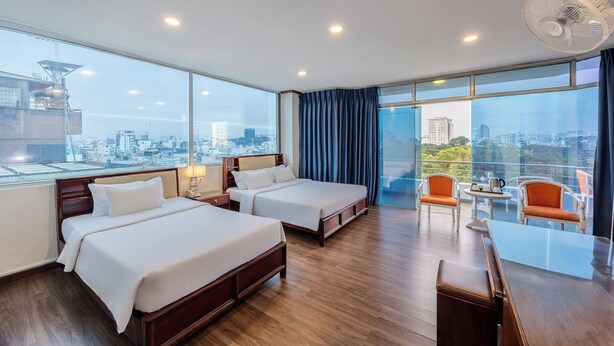 A hotel room with two beds, a balcony with a table and chairs, and a city view.