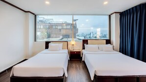 A hotel room with two beds, a large window with a city view, and a nightstand with a lamp.