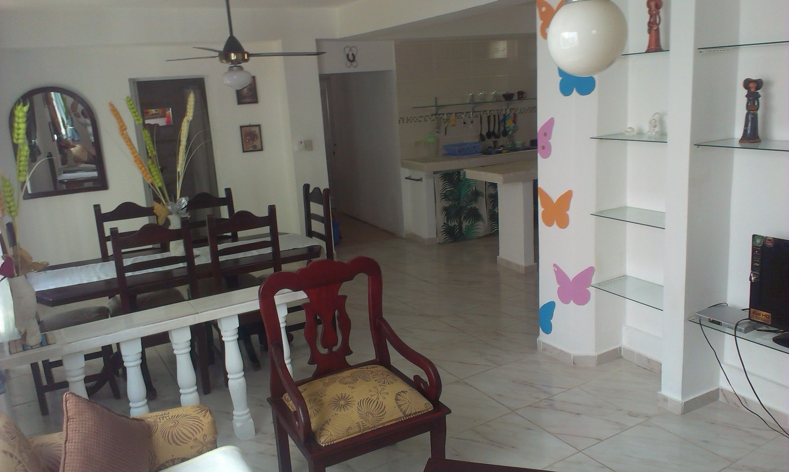 A dining area with a wooden table and chairs, a ceiling fan, and a kitchen in the background.