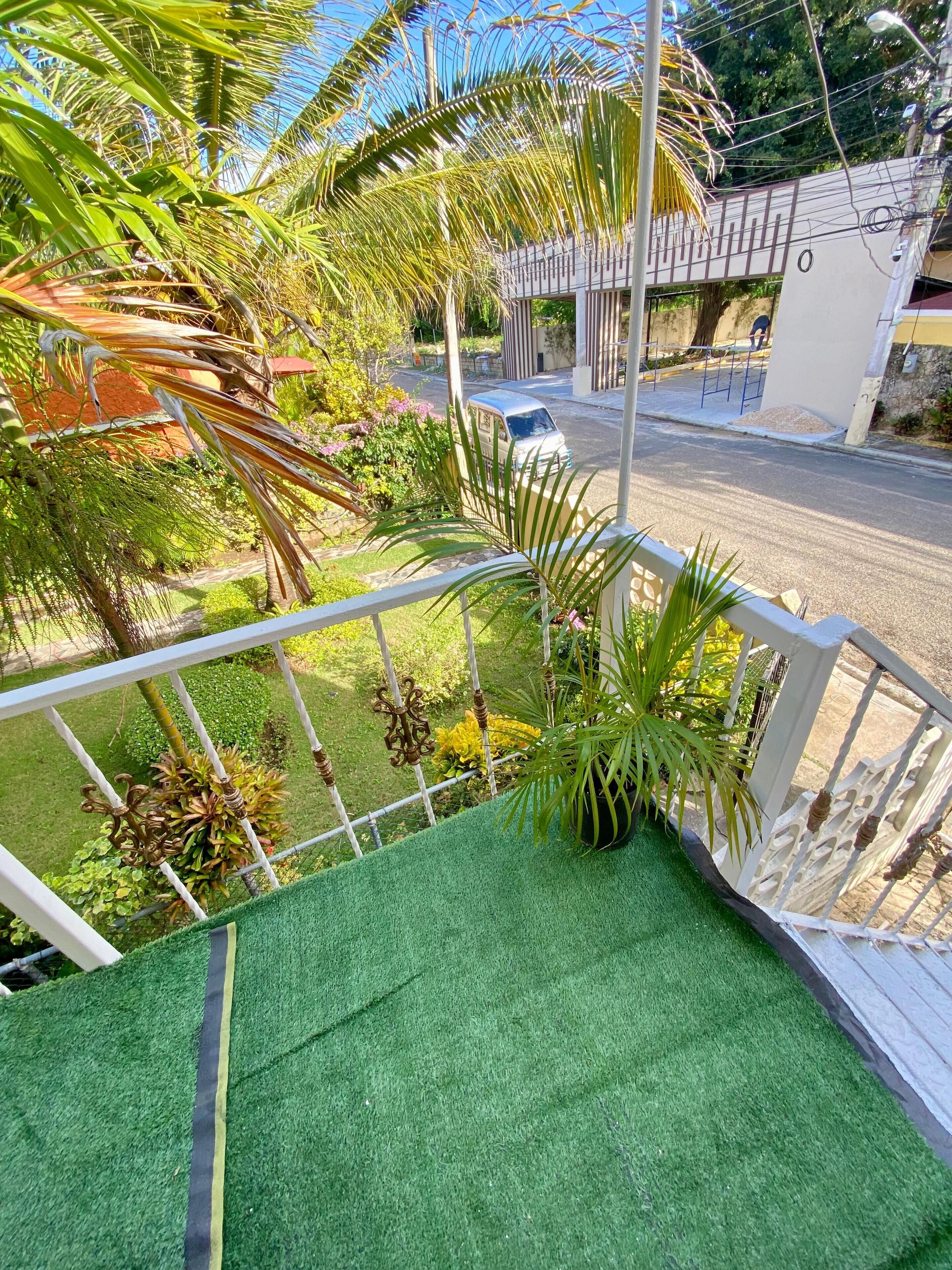Ein Balkon mit Blick auf eine Straße, Grünflächen und einen weißen Zaun.