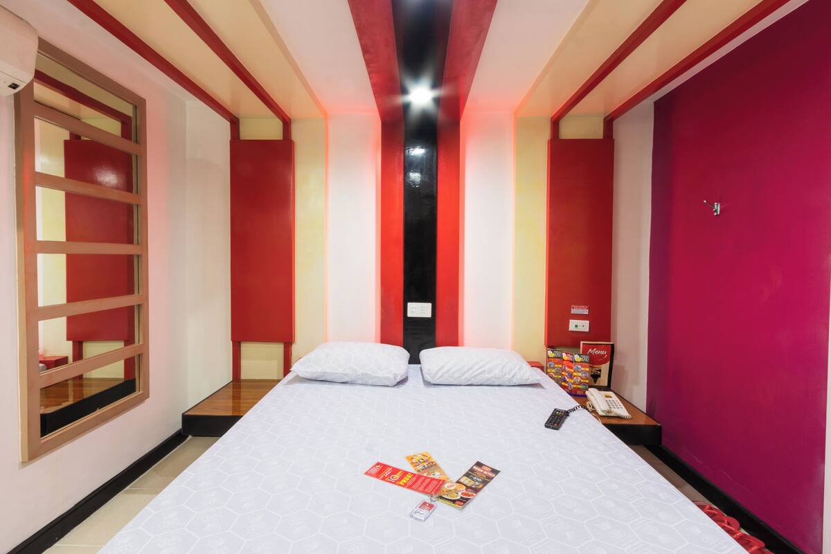 Une chambre d’hôtel avec un grand lit, deux oreillers, une table de chevet avec un téléphone et une fenêtre donnant sur l’extérieur.