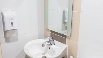 A bathroom with a white sink, a mirror, and a soap dispenser.