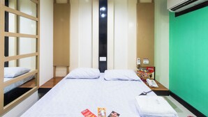 A hotel room with a bed, pillows, a bedside table with a phone and magazines, a green wall, and an air conditioning unit. - Hotel Sogo Kalentong Marketplace (Mandaluyong)