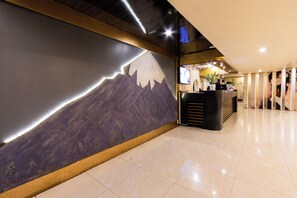 Un hall d’hôtel agrémenté d’une fresque représentant une montagne, un comptoir d’accueil et un aménagement intérieur moderne.