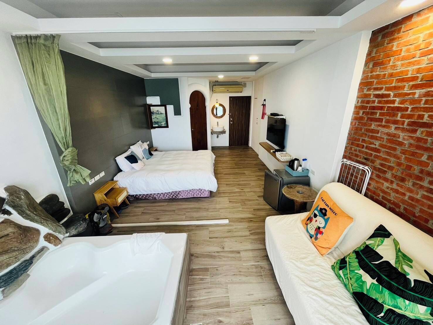 A hotel room with two beds, a sofa, a TV, and a brick wall.