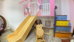 A children's playroom with a wooden slide, a Hello Kitty wall decoration, a large stuffed dog, and a blue and yellow storage unit. - Rockhand Homestay (Hengchun)
