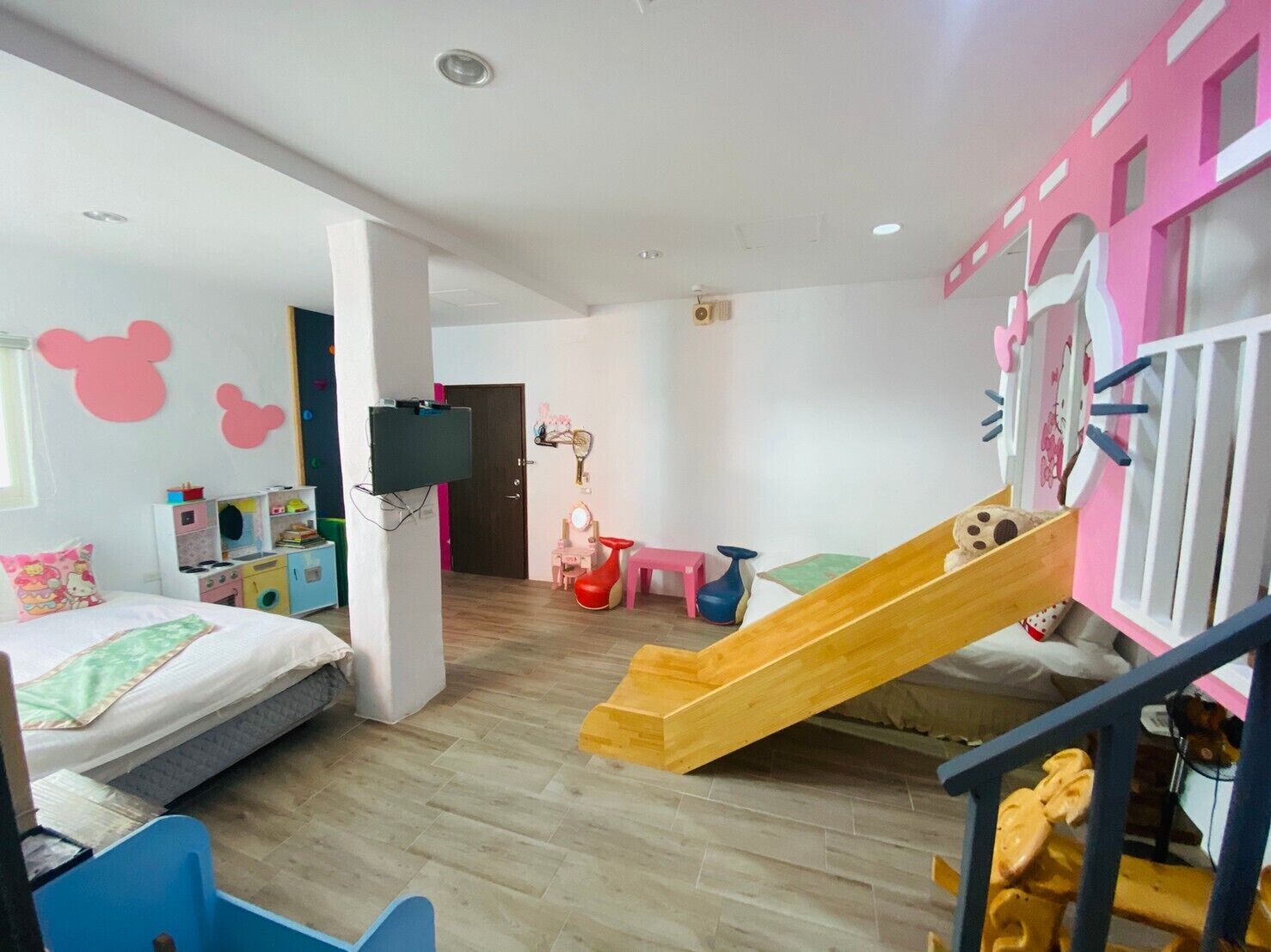 Habitación para niños con cama, zona de juegos con un tobogán, televisor montado en la pared y decoración rosa en la pared.