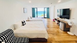 A modern hotel room with two beds, a TV, a fan, and a view of the ocean. - Rockhand Homestay (Hengchun)