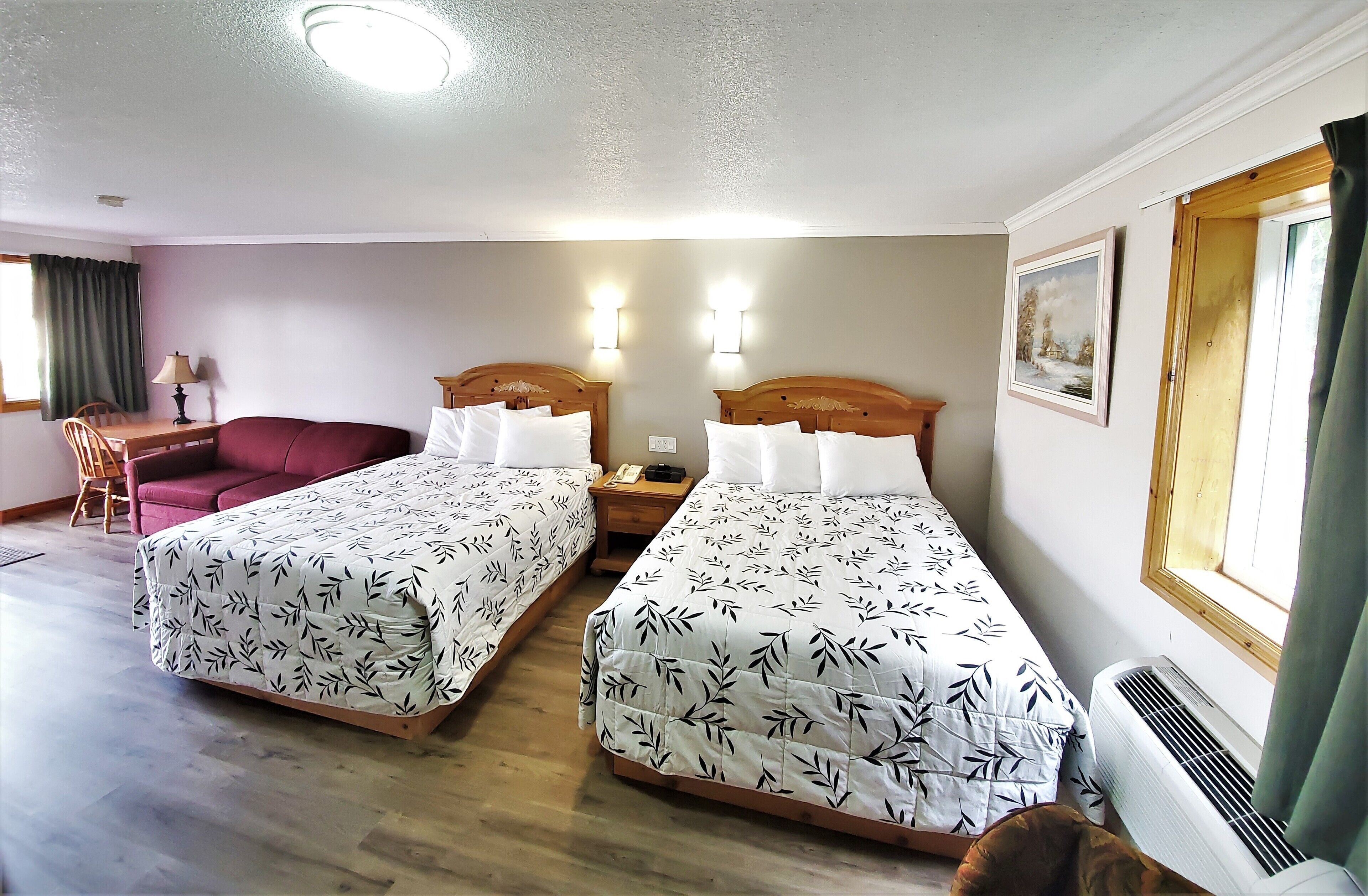 A hotel room with two beds, a red sofa, a wooden nightstand with a phone, and a window with curtains.