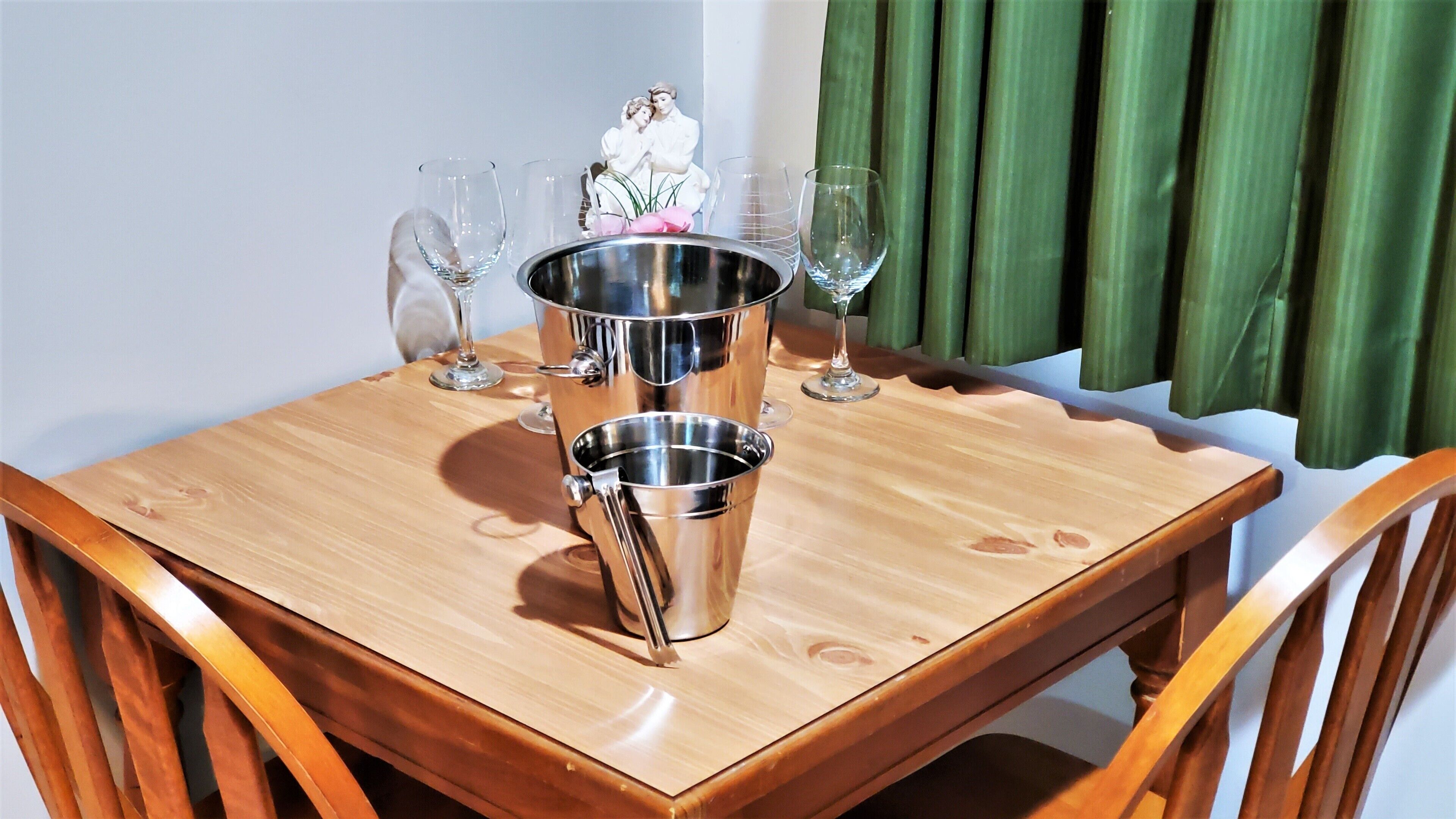 Uma mesa de madeira com um balde metálico e vários copos de vinho, em frente a um fundo de cortina verde.
