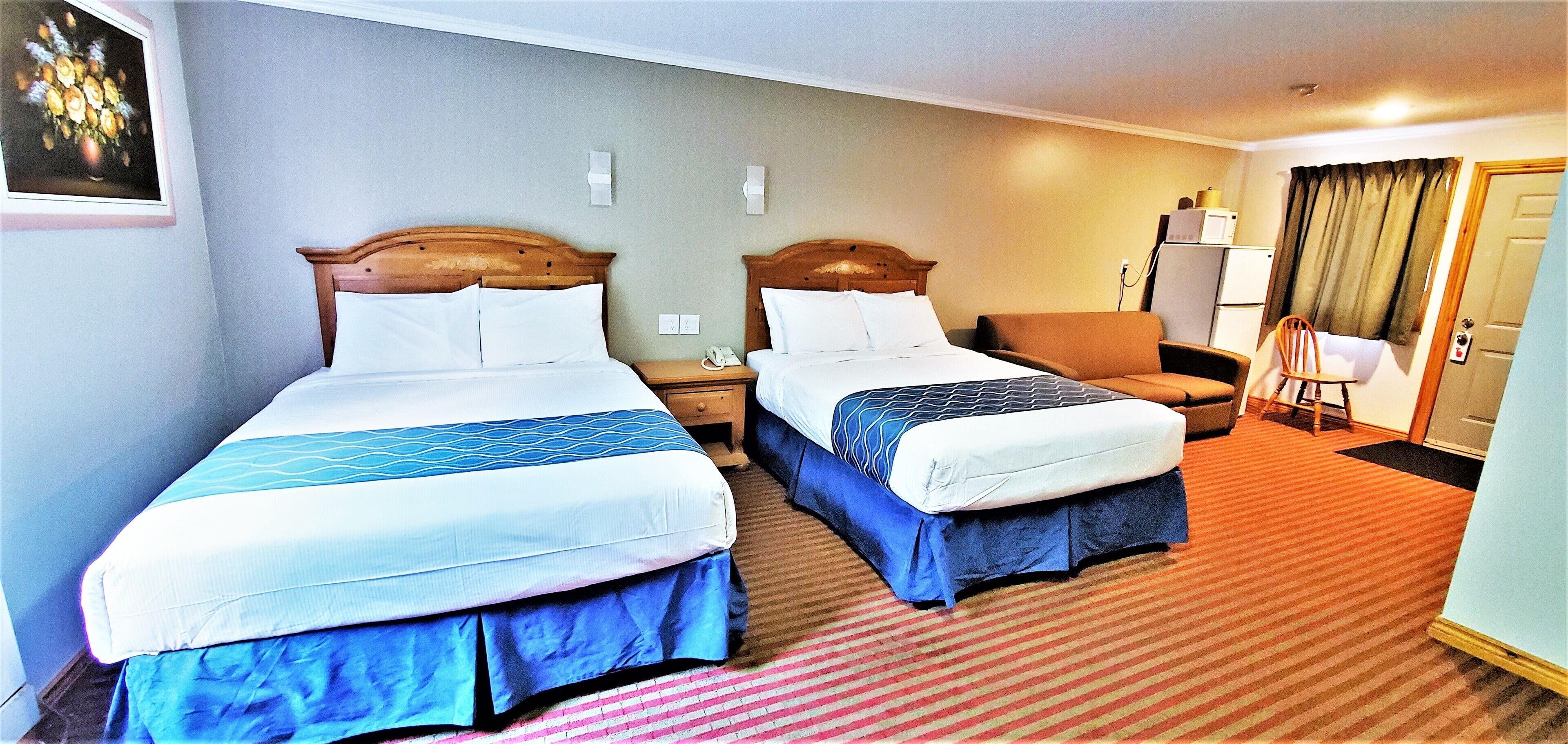 A hotel room with two beds, a desk, a chair, and a small kitchenette.