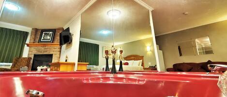 Una habitación de hotel con una bañera roja grande, una chimenea, un televisor y una cama con cabecera.