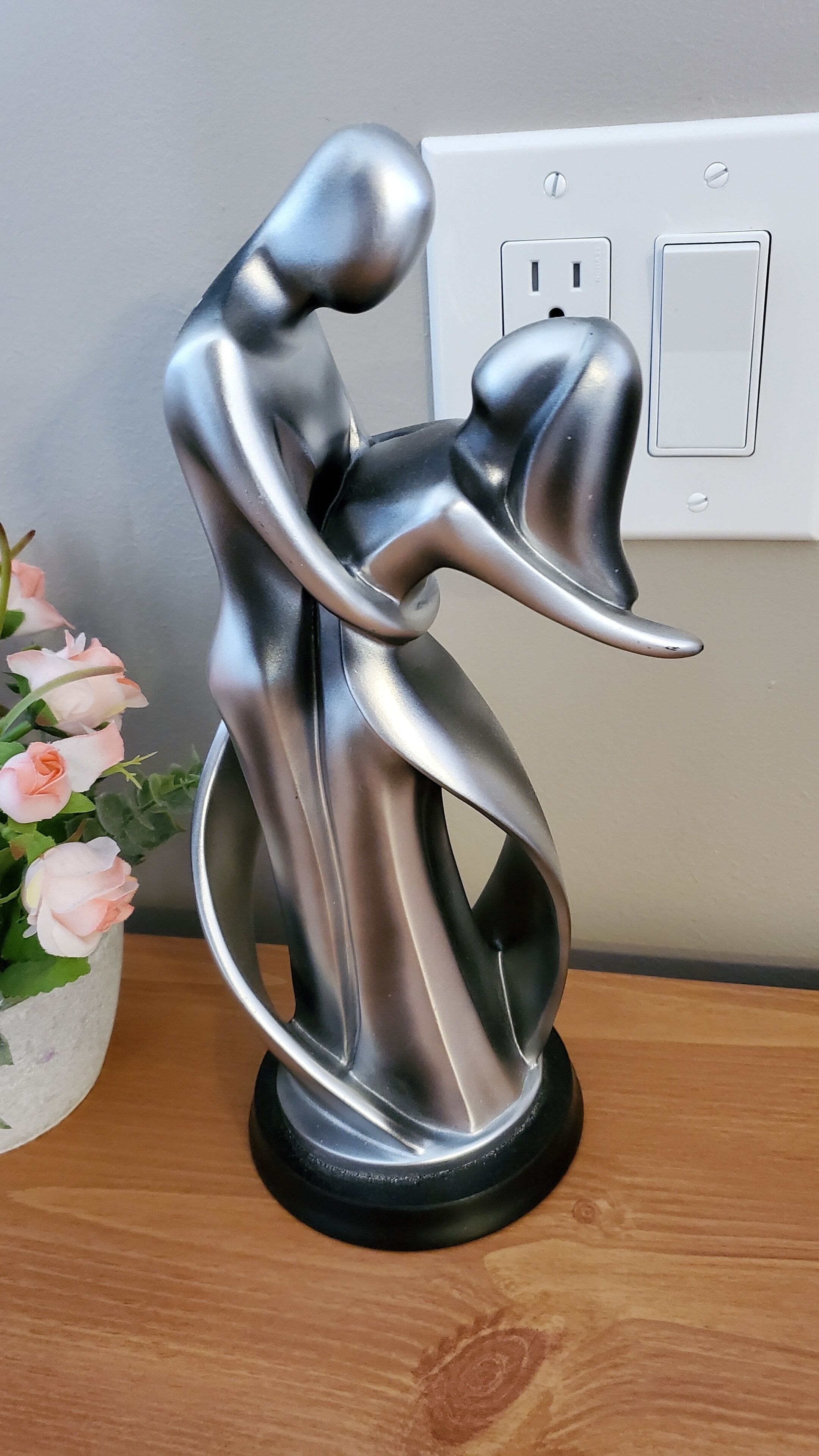 Una escultura metálica de una pareja en una pose dinámica sobre una superficie de madera.