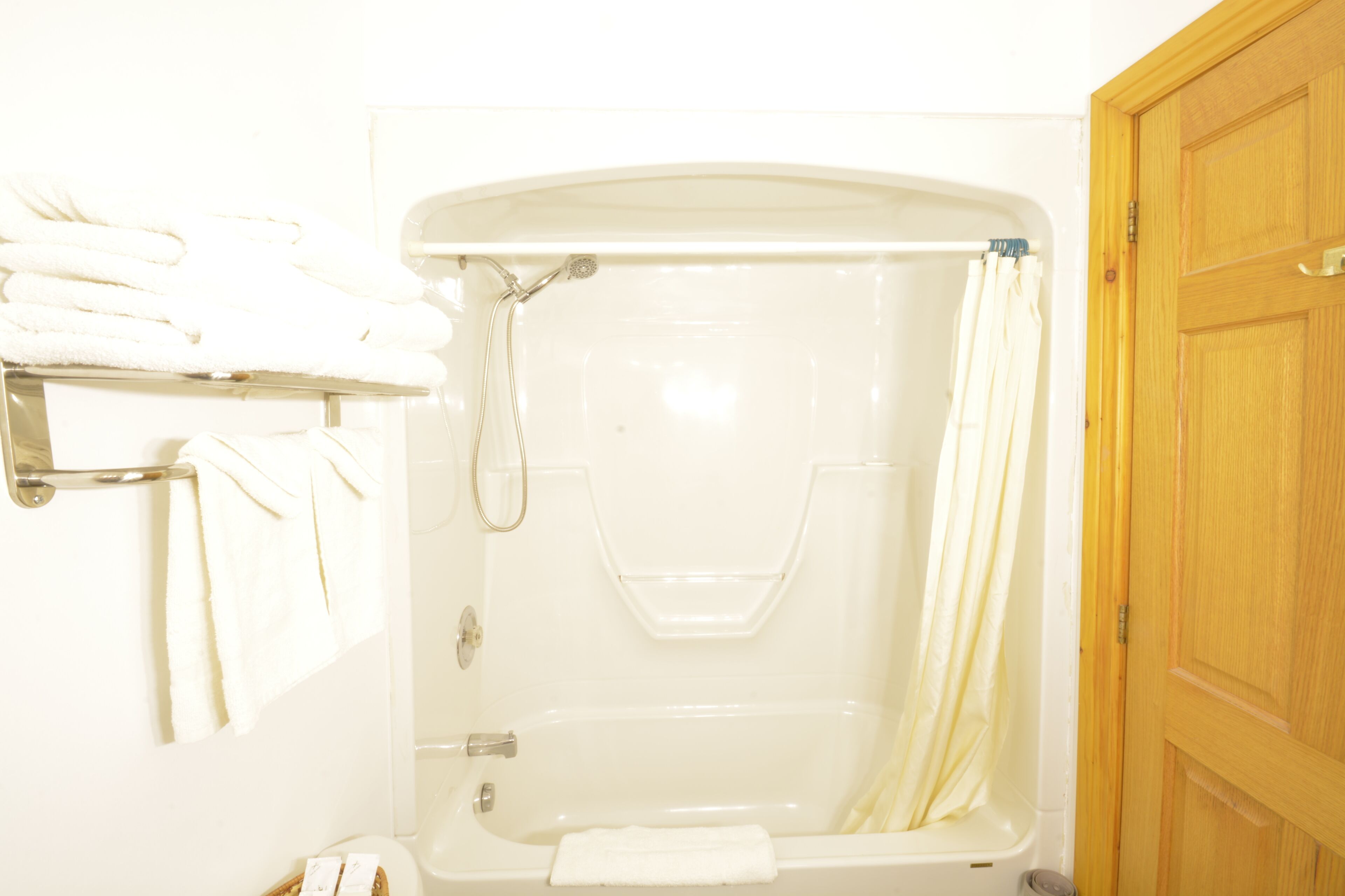 A bathroom with a bathtub, a shower curtain, and a stack of white towels on a rack.