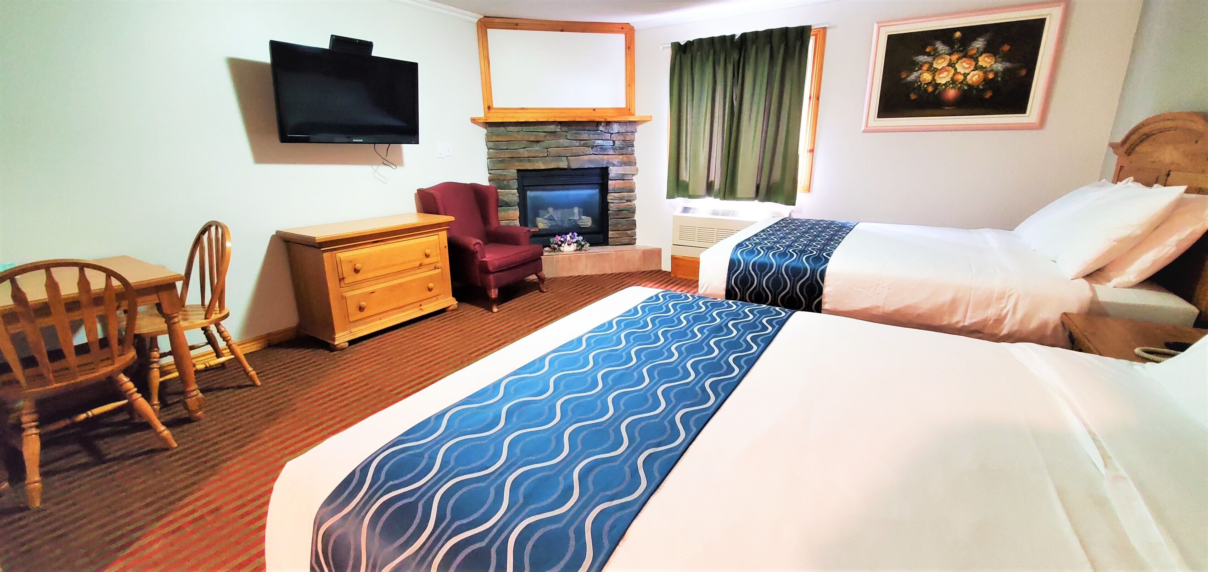 A hotel room with a bed, a chair, a dresser, a television, a fireplace, and a painting on the wall.