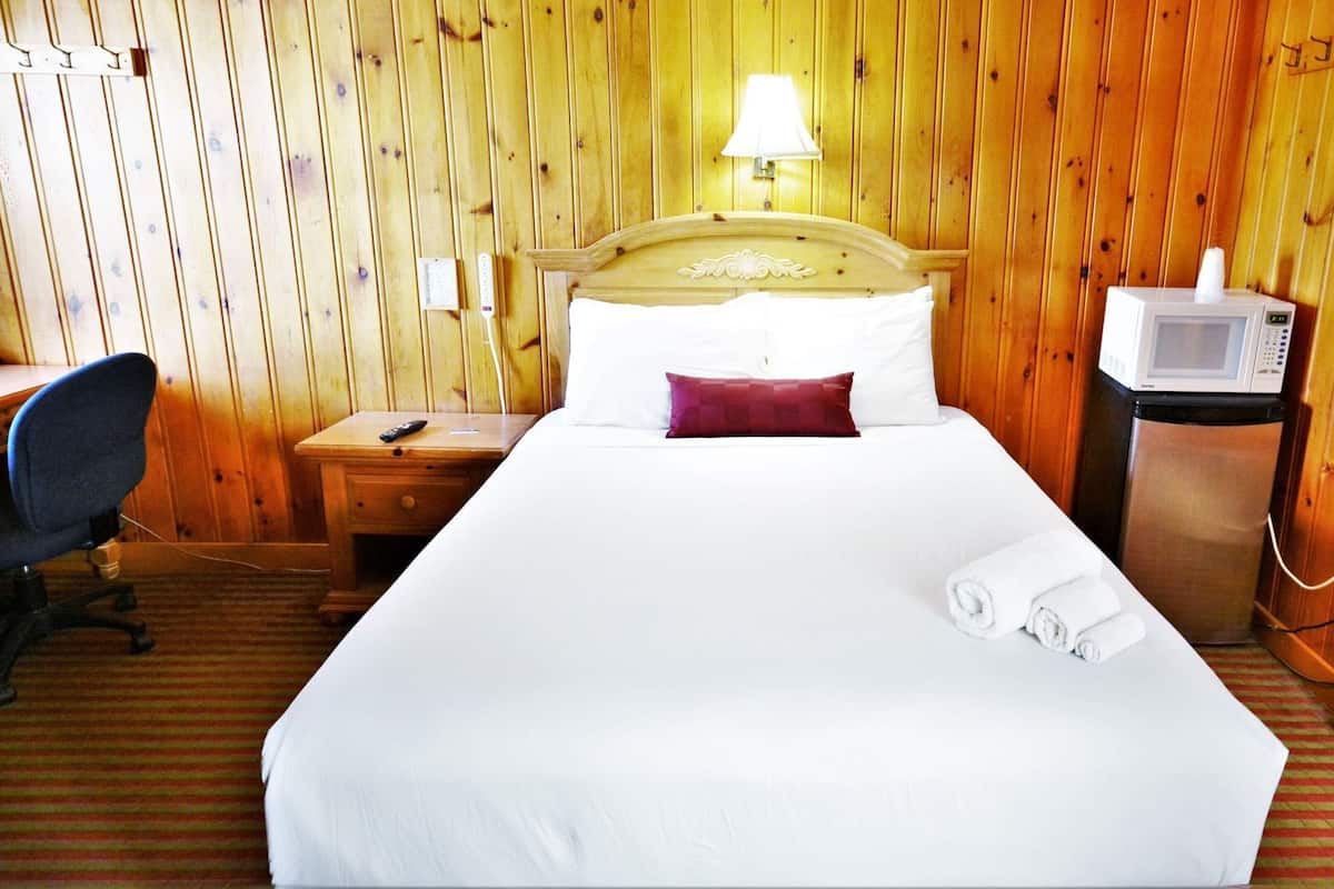 A hotel room with a bed, a desk with a chair, a microwave, and a lamp.