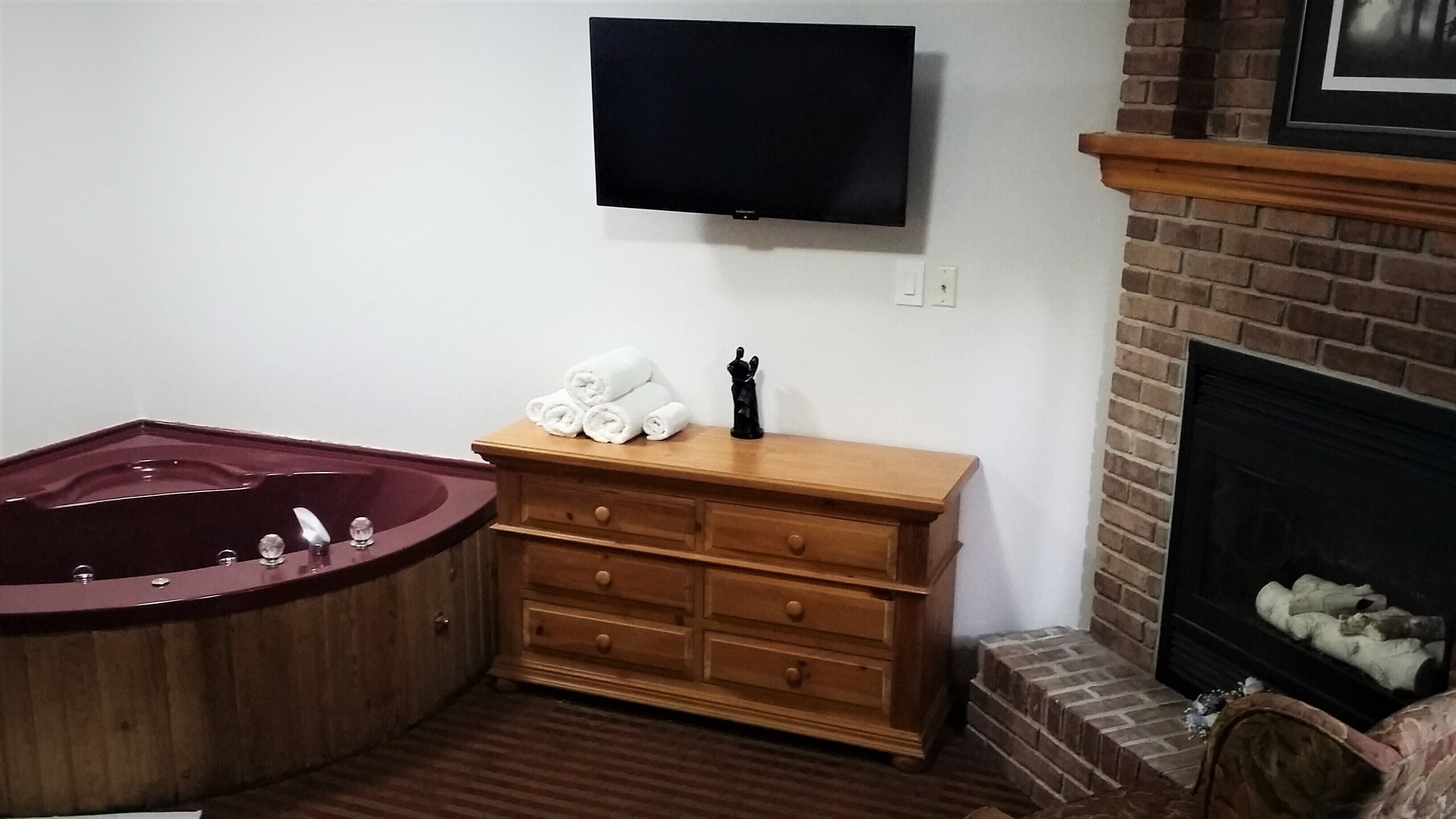 Un baño con bañera, tocador de madera, televisor de pantalla plana y chimenea.