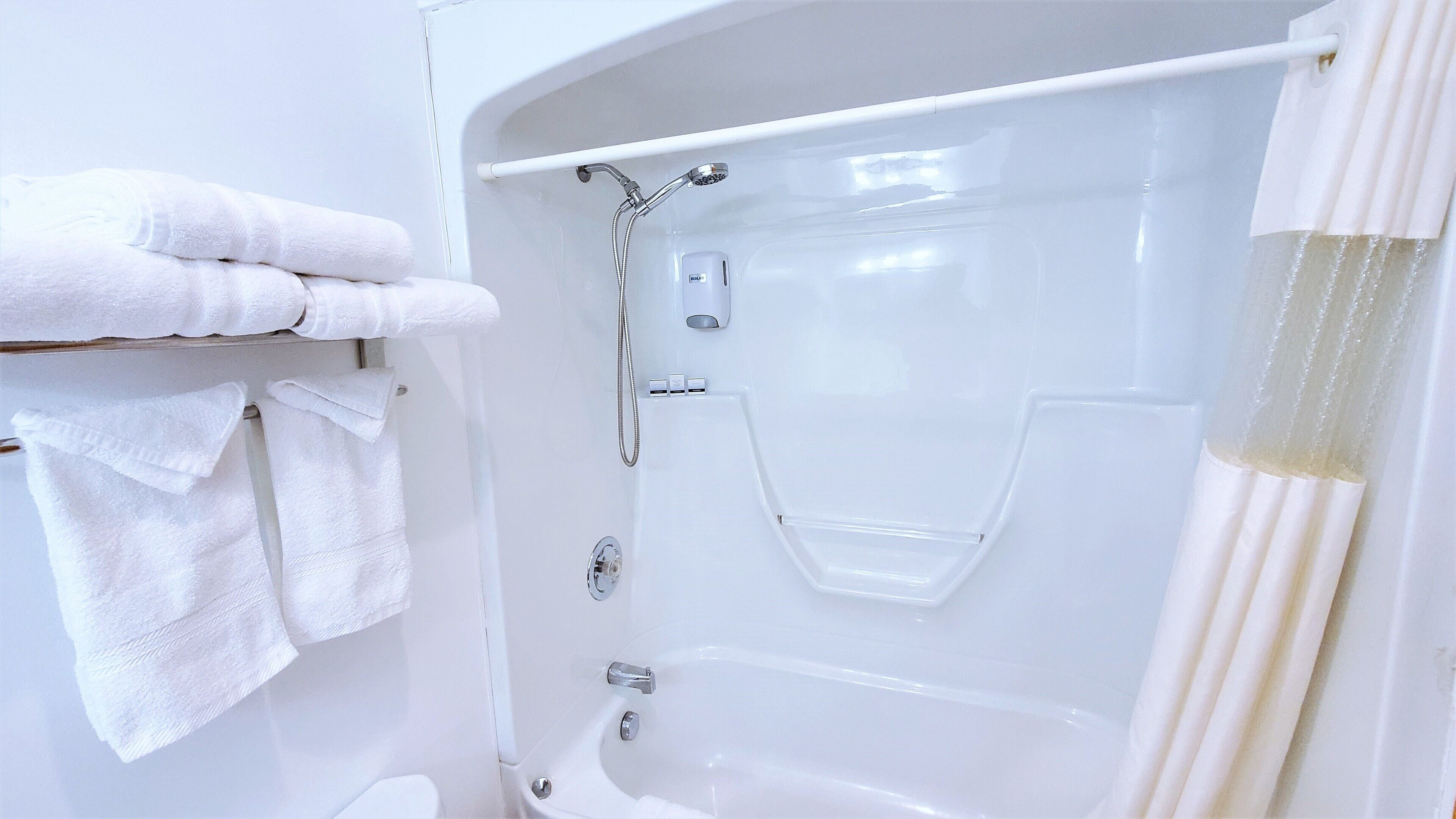 A white bathtub with a shower head, a towel rack with towels, and a curtain.