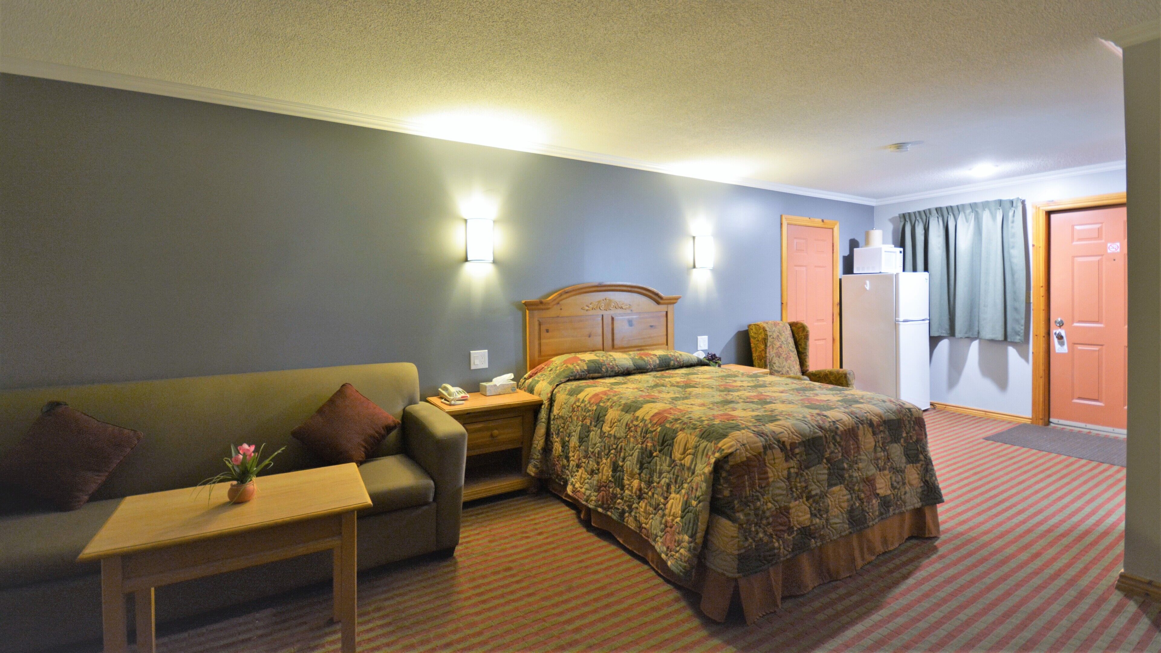 A hotel room with a bed, a sofa, a small table, a nightstand, and a door.