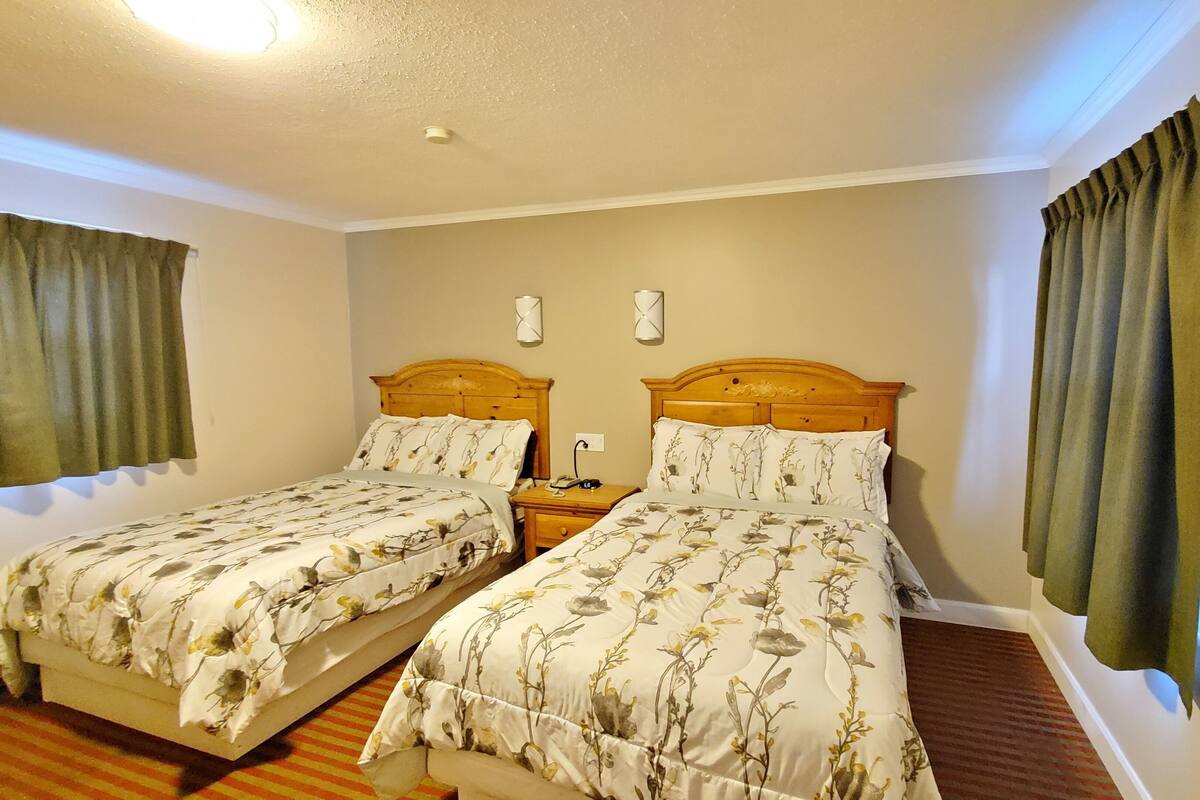 A twin room with two single beds, a nightstand with a lamp, and a wall-mounted light fixture.