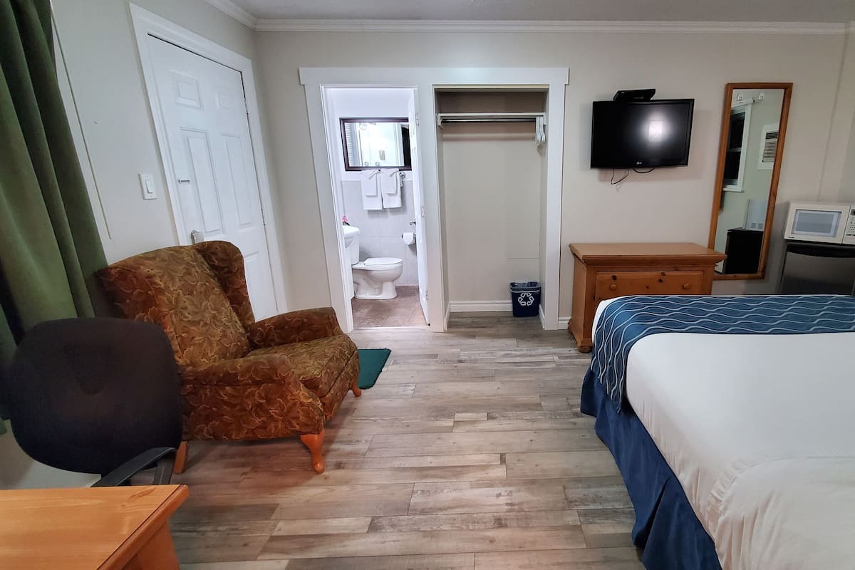 A hotel room with a bed, a chair, a television, a dresser, and a bathroom visible through an open door.