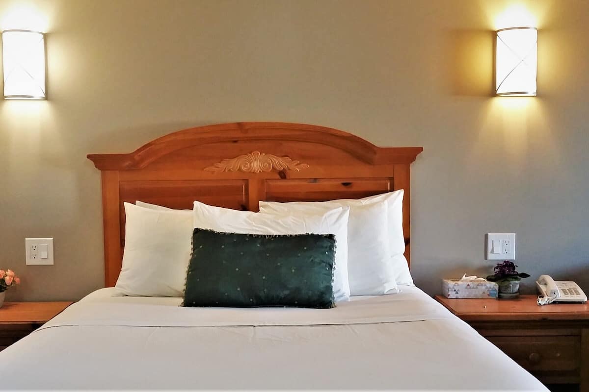 A neatly made bed with white and green pillows, a wooden headboard, and two bedside tables with lamps and a phone.