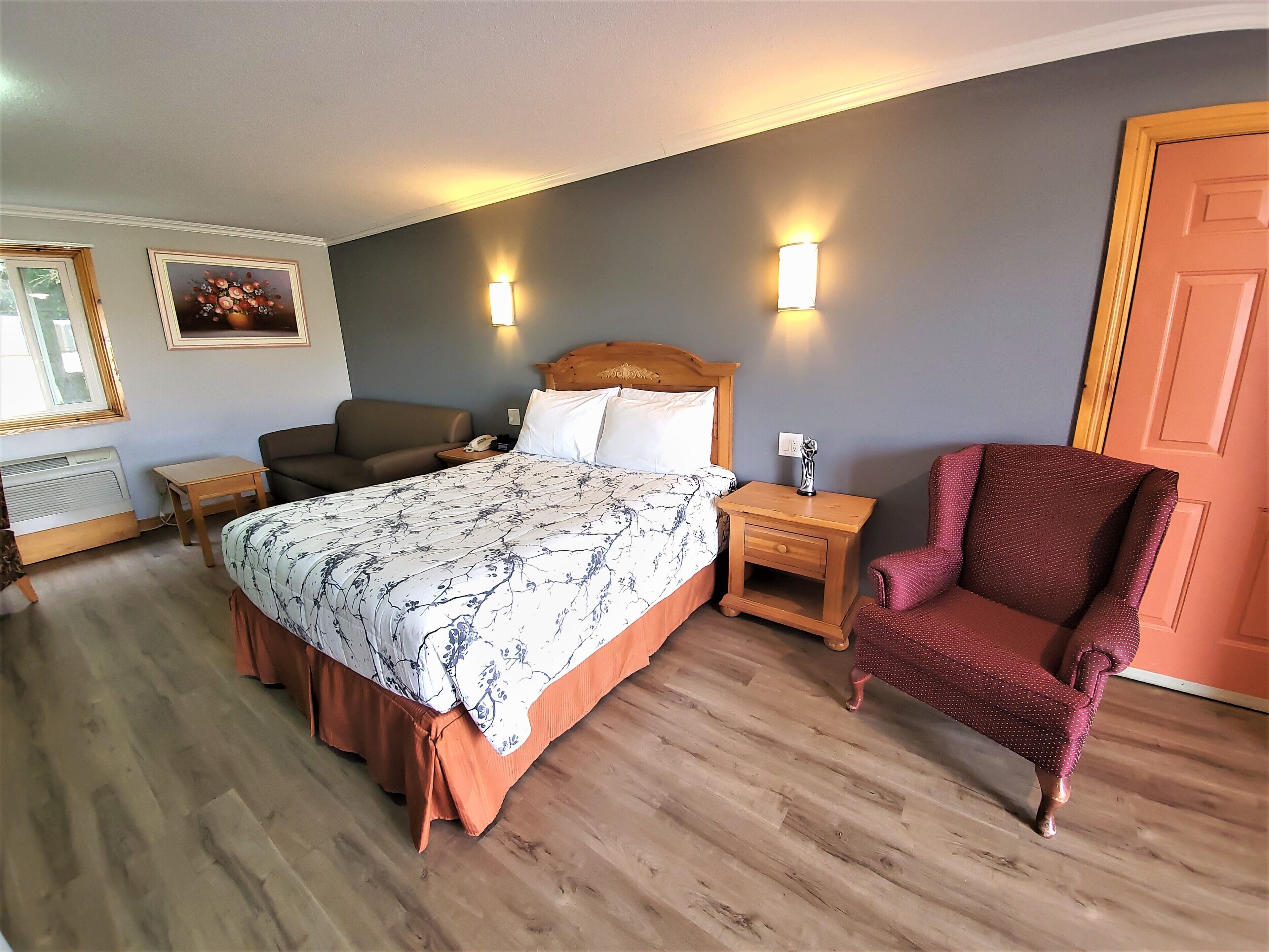 A hotel room with a large bed, a wooden nightstand, a red armchair, and a wall-mounted lamp.