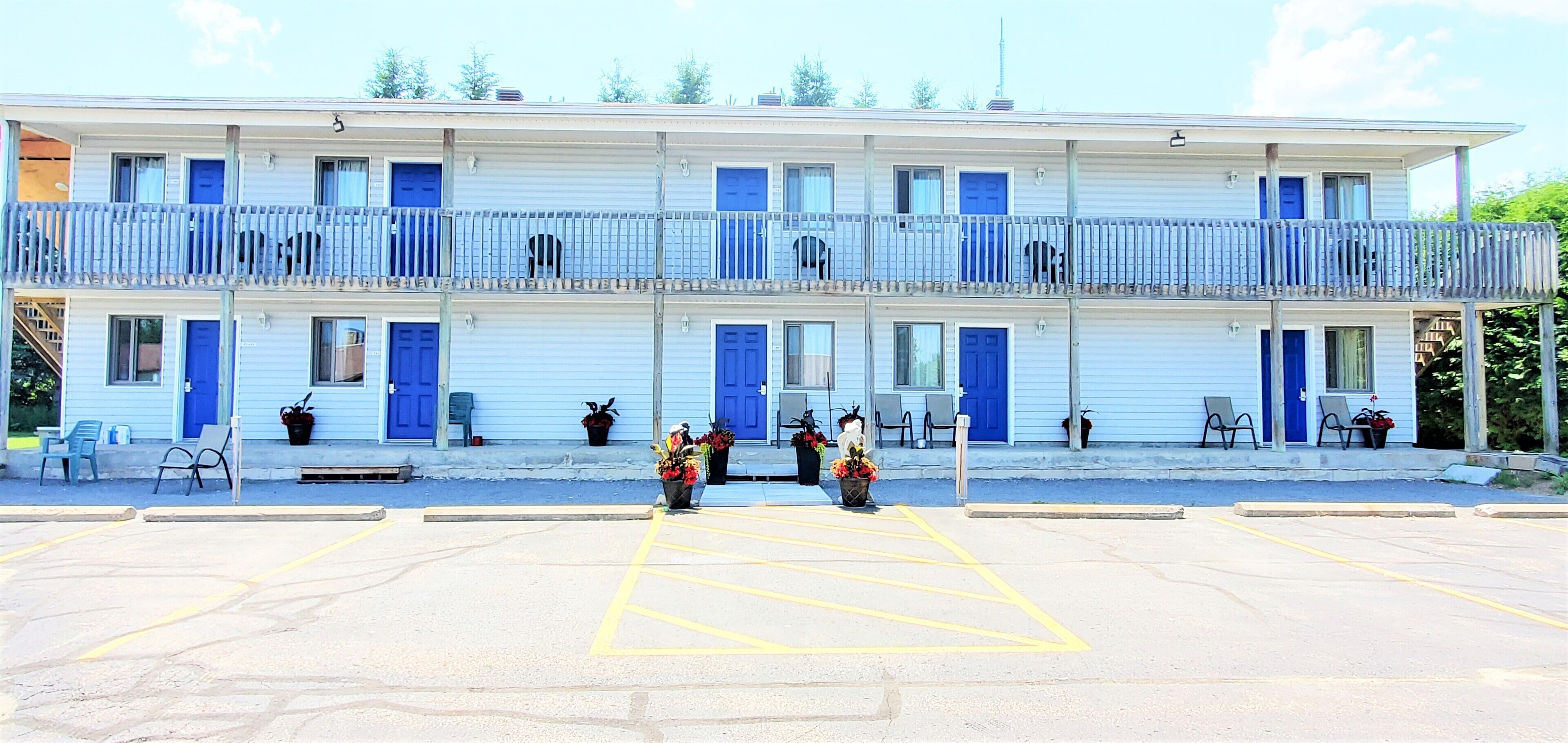 Een gebouw met twee verdiepingen, blauwe deuren en ramen, een overdekte parkeerplaats en terrasjes.