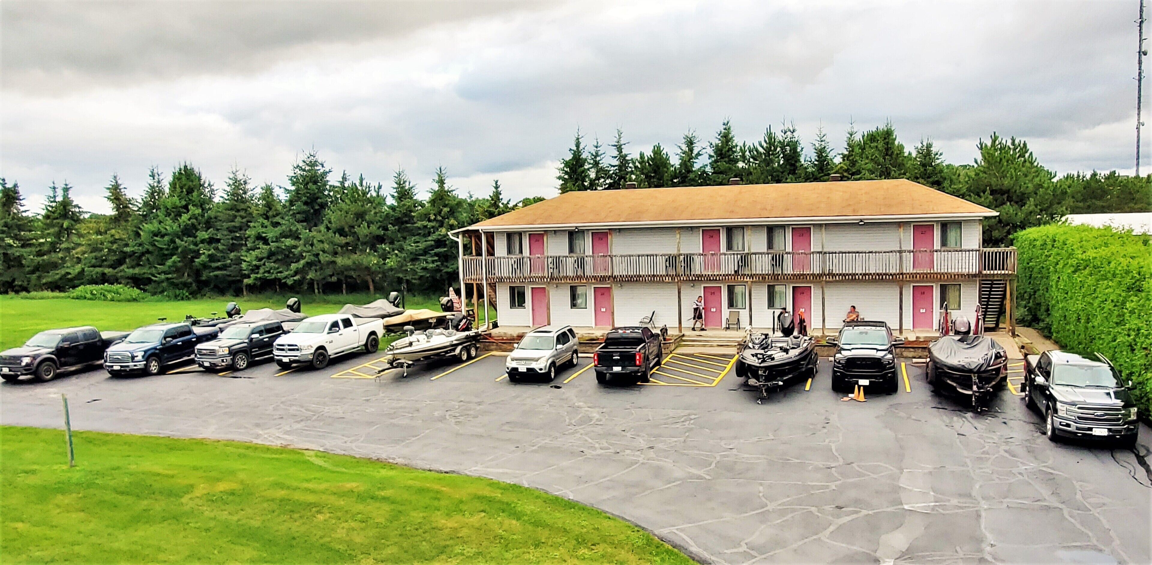 A motel with a two-story structure, a covered parking area, and a row of vehicles parked in front.
