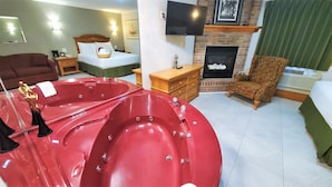Ein Zimmer mit einer großen, roten Whirlwanne, einem Bett mit weißer Bettwäsche, einer Holzkommode, einem an der Wand befestigten Fernseher und einem Kamin.