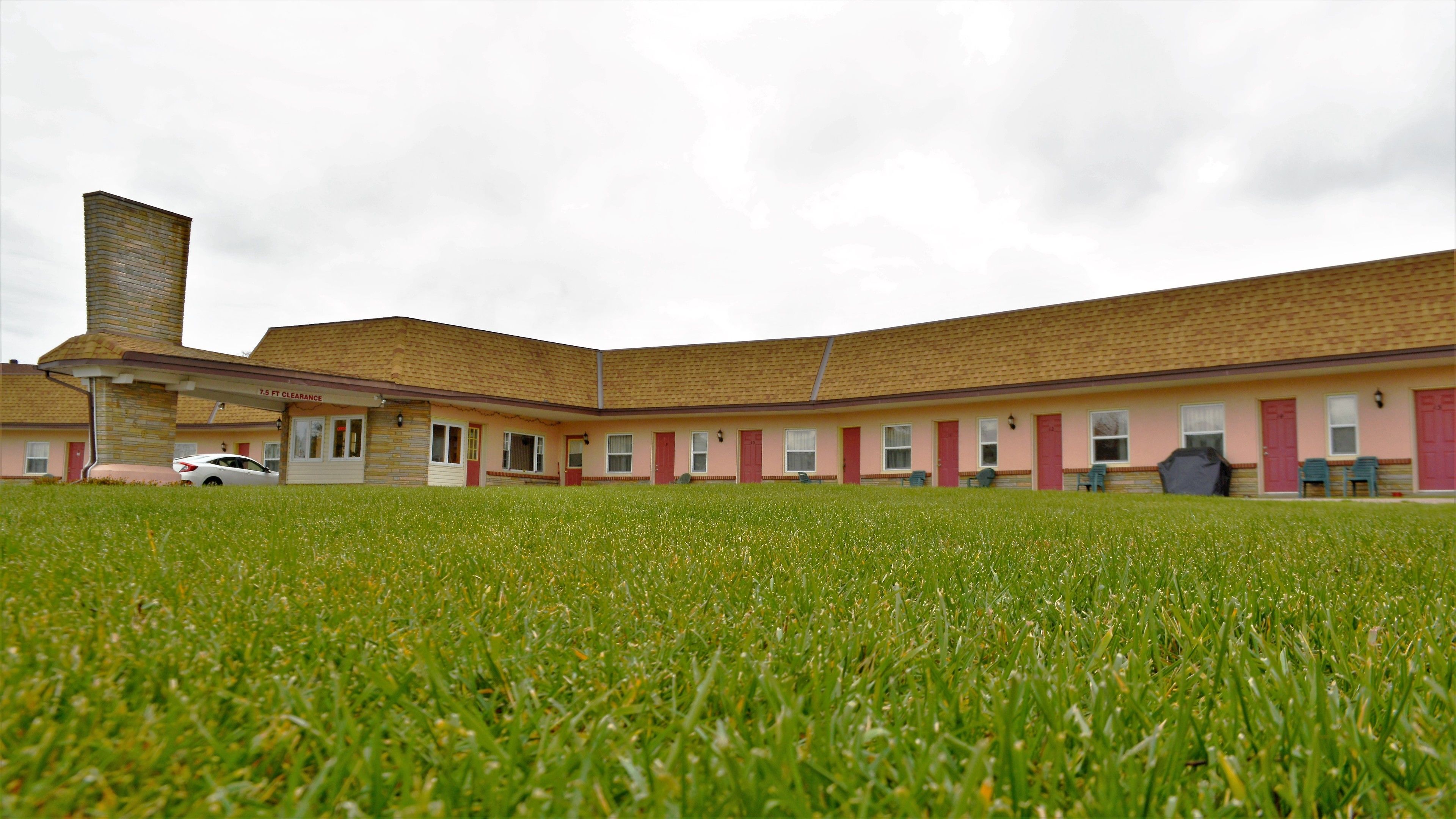 A motel with a covered parking area and a grassy lawn in front.