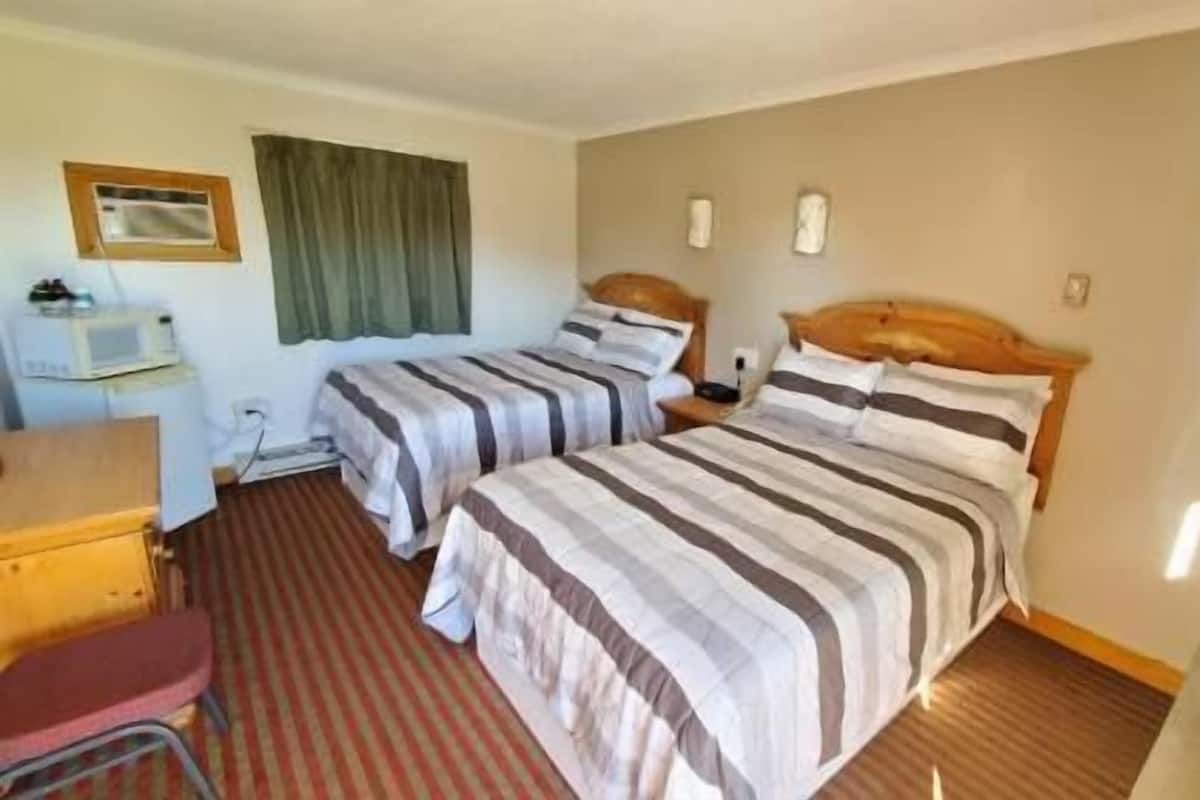 A hotel room with two beds, a desk, a chair, a television, and a window with curtains.