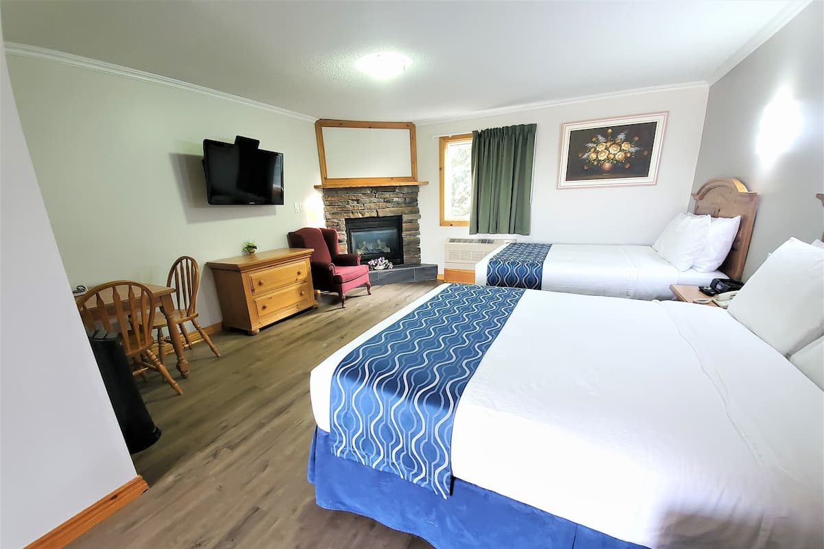A hotel room with two beds, a TV, a fireplace, a dining area with chairs, and a wooden dresser.