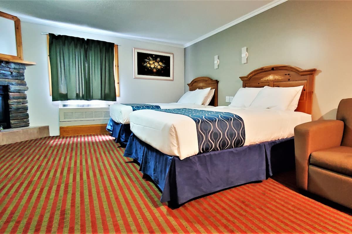 A hotel room with two beds, a sofa, a fireplace, and a framed picture on the wall.