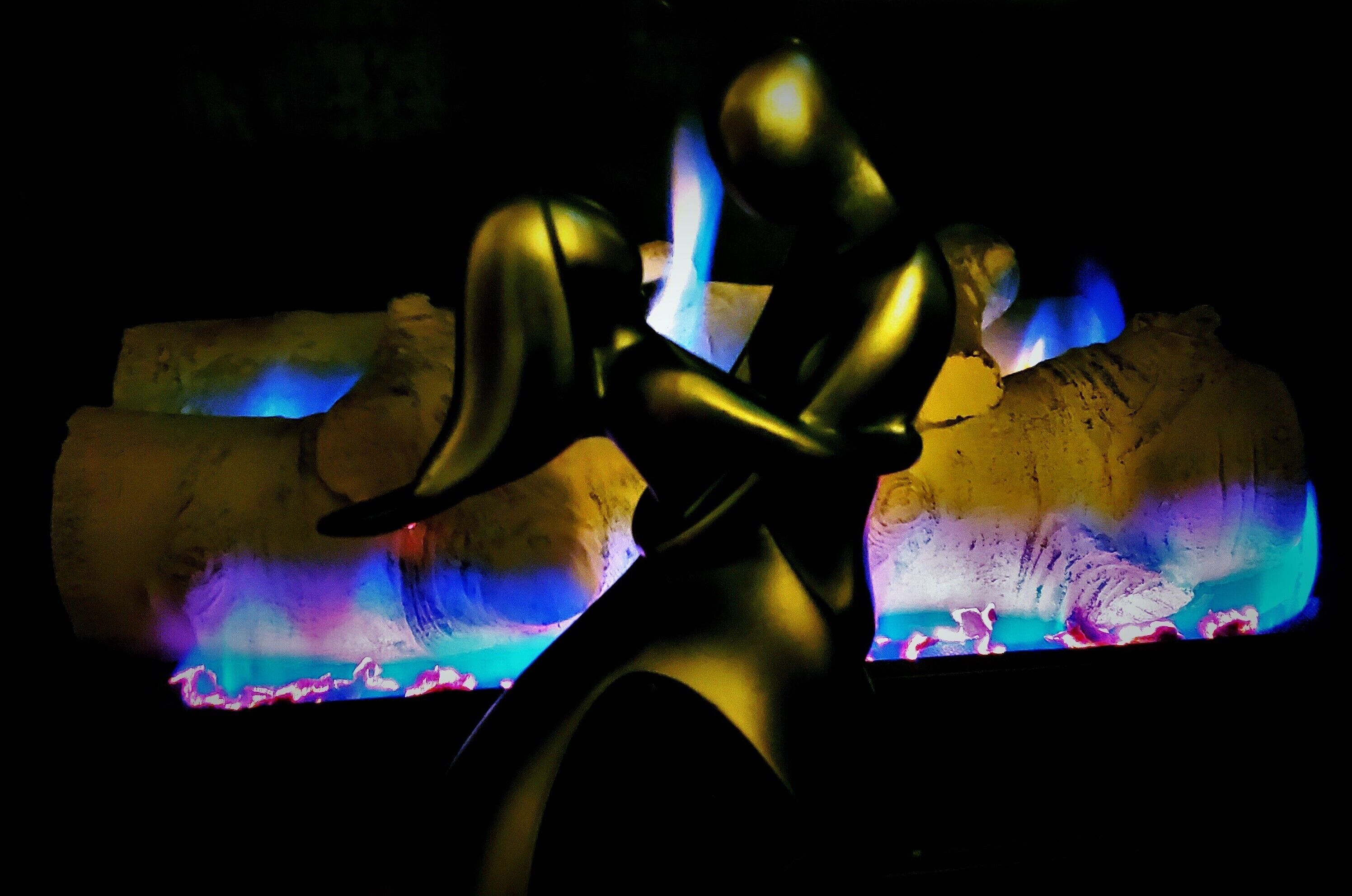 Uma escultura em um ambiente escuro com um colorido espetáculo de luz ao fundo.