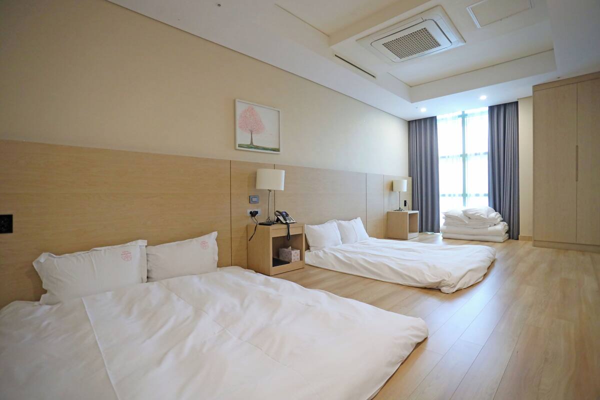 A hotel room with two beds, a bedside table with a lamp, a phone, and a window with curtains.