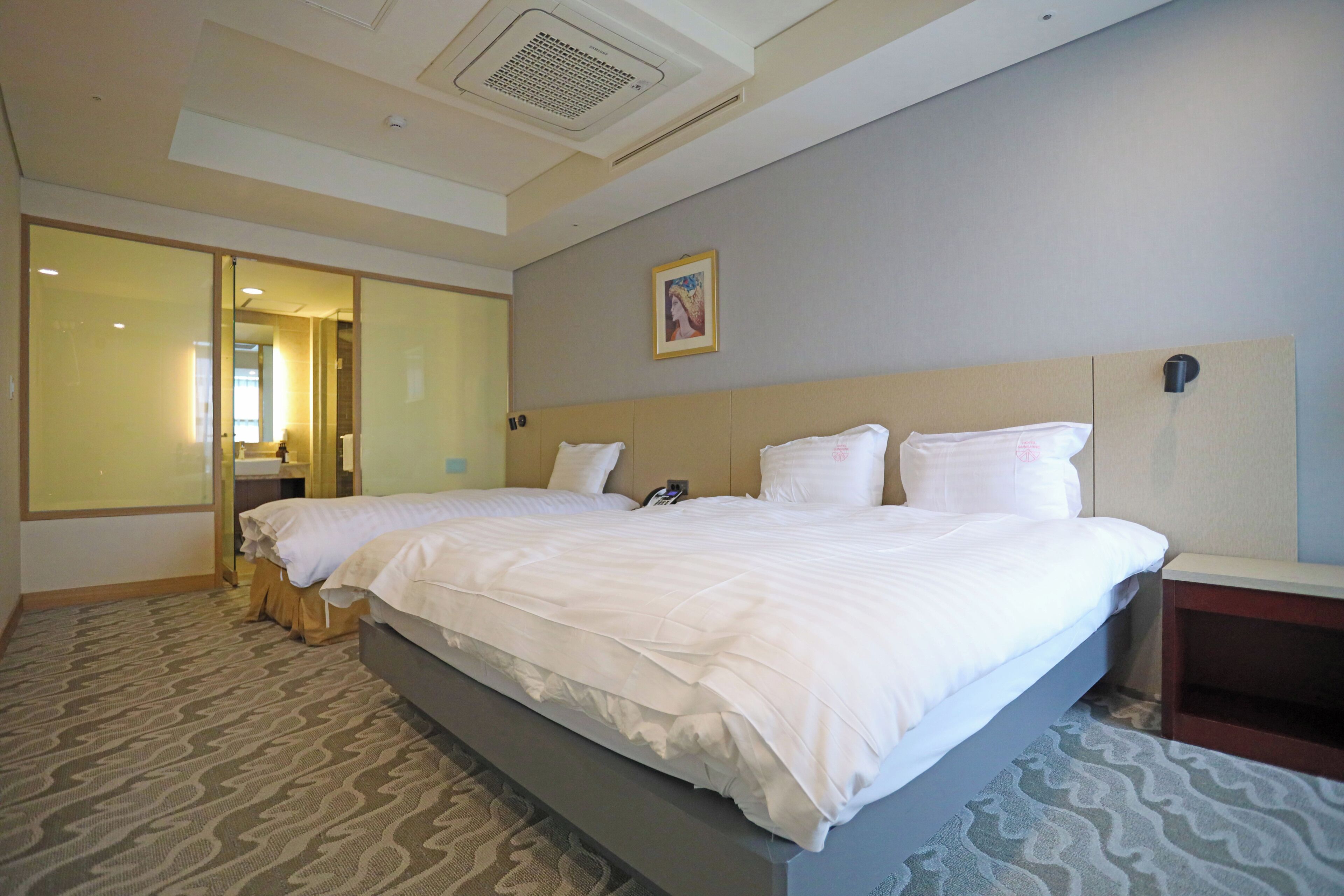 A hotel room with a large bed, a bedside table, a wall-mounted phone, and a picture on the wall.
