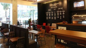 A modern cafe interior with tables and chairs, a blackboard menu, and a TV screen. - Sunshine Hotel (Daejeon)