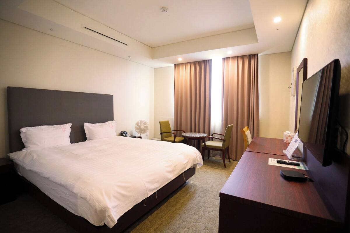 A hotel room with a large bed, a desk with a computer, a chair, and a TV.