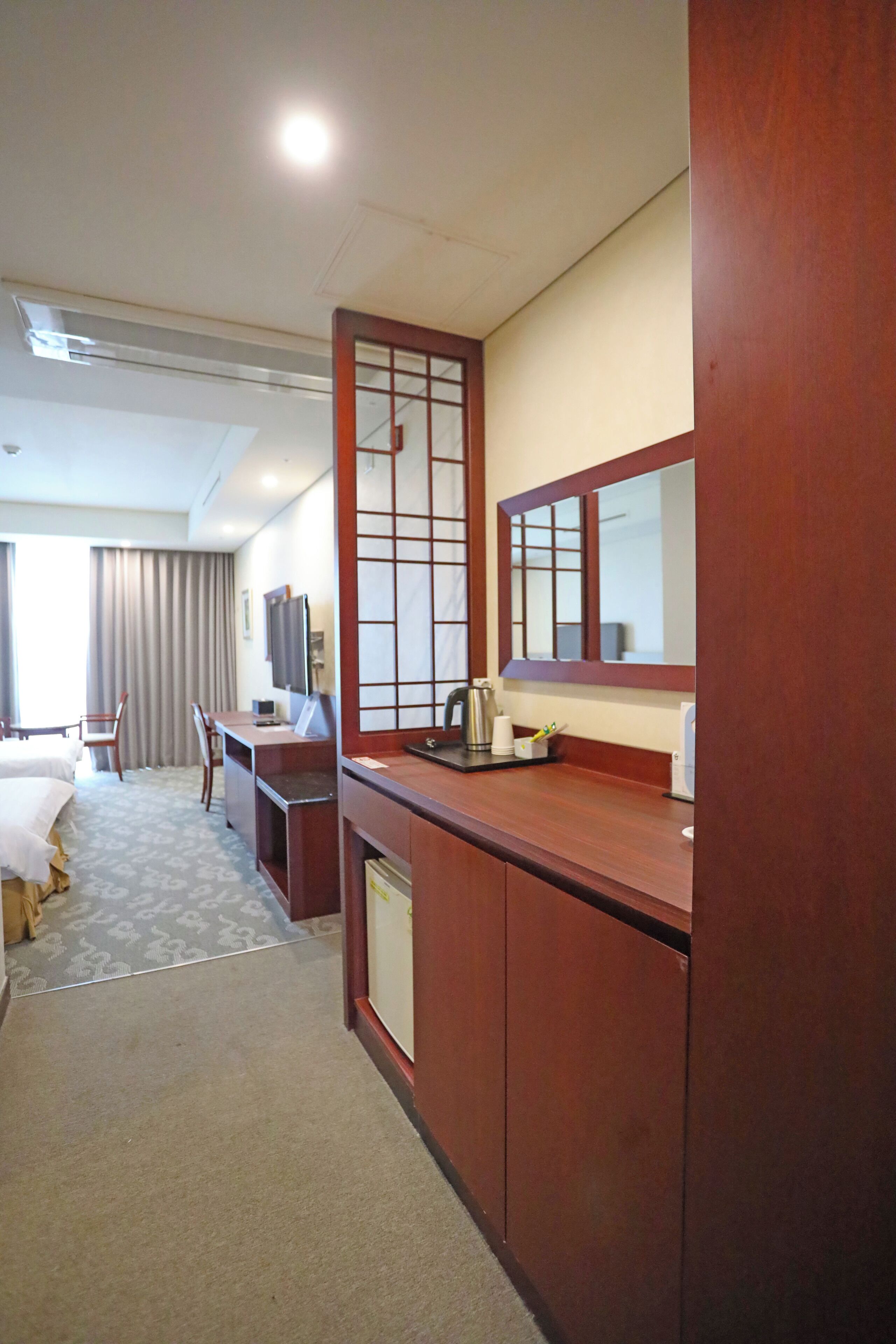 A hotel room with a bed, desk, chair, and a large mirror.